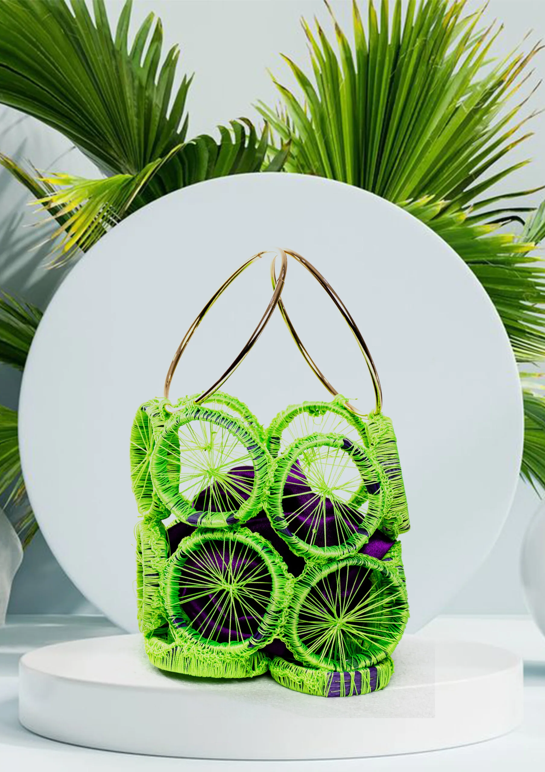 3 Vue de face du sac à main tressé en disques vert fluo avec tissu violet visible et anses anneaux dorés, fond de feuilles de palmier