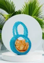 Vue de face du sac à main rond en perles bleu saphir avec doublure satin doré, fond de feuilles de palmier