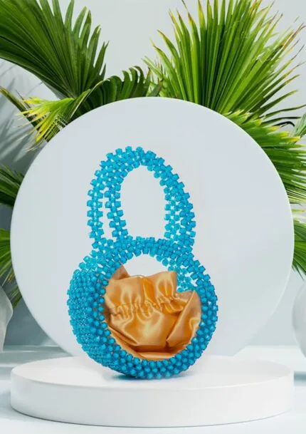 Vue de face du sac à main rond en perles bleu saphir avec doublure satin doré, fond de feuilles de palmier