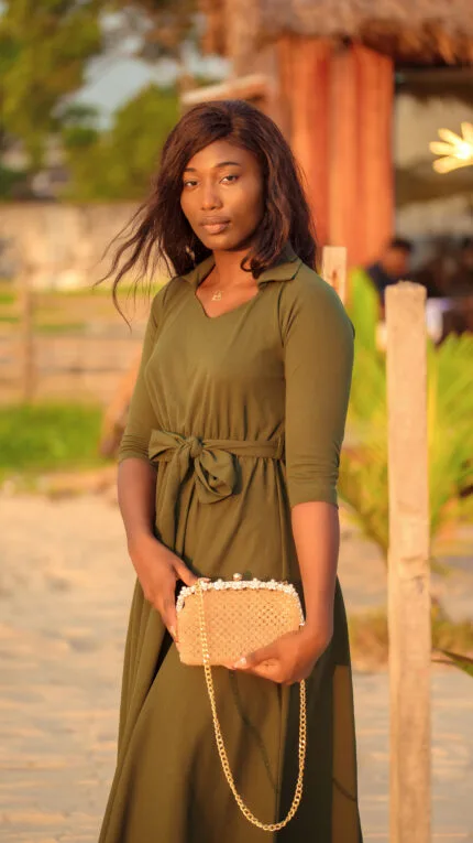 Mannequin en robe verte tenant le sac à main perlé nude rose à chaîne dorée, sur fond de plage