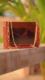 Vue de face du sac à main perlé ambre à façade brillante, posé sur un banc en bois
