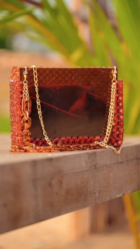 Vue de face du sac à main perlé ambre à façade brillante, posé sur un banc en bois
