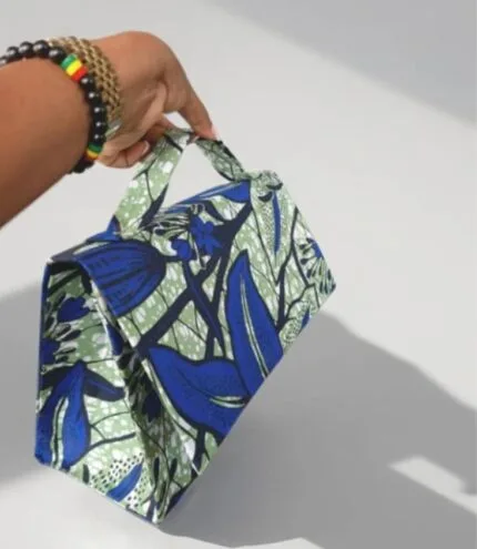 Sac à main en tissu wax bleu, vert et blanc tenu à la main, fond blanc studio