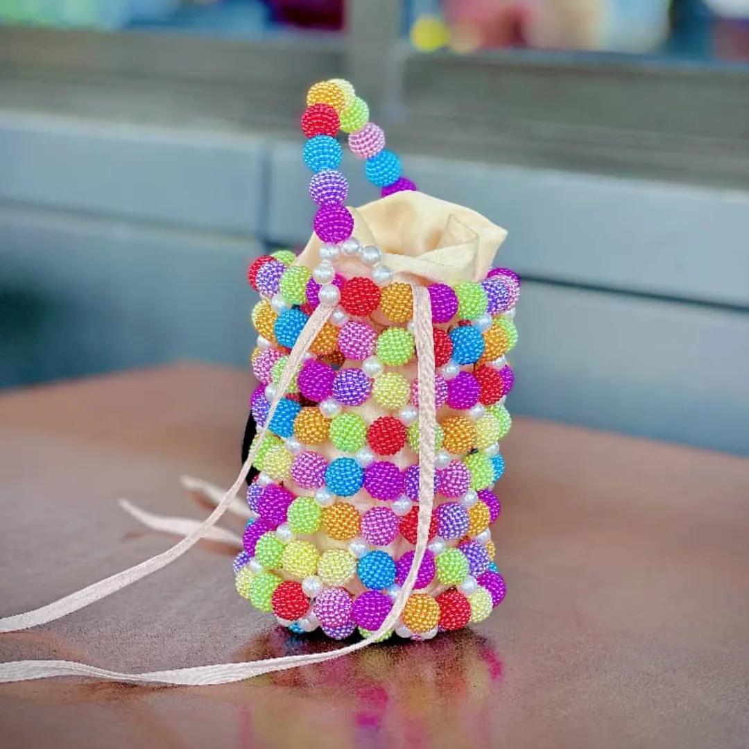 Sac à main Kalunga-2 Vue de face du mini sac seau perlé multicolore à doublure satin crème, posé sur une table en bois
