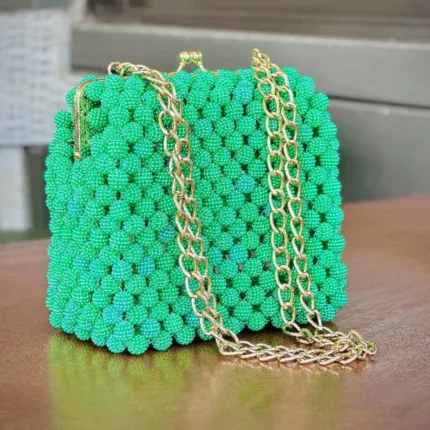 Vue de face du sac à main perlé vert émeraude à fermoir et double chaîne dorée, posé sur une table en bois