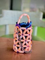 Vue de profil du mini sac perlé rose pêche et violet à chaîne argentée, posé sur une table