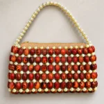 Vue de face du sac Malika Kongo sur fond beige, perles marron et dorées en quadrillage, fermeture zippée