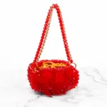 Vue de face du sac à main perlé rouge à franges de plumes et doublure satin doré, fond marbre blanc