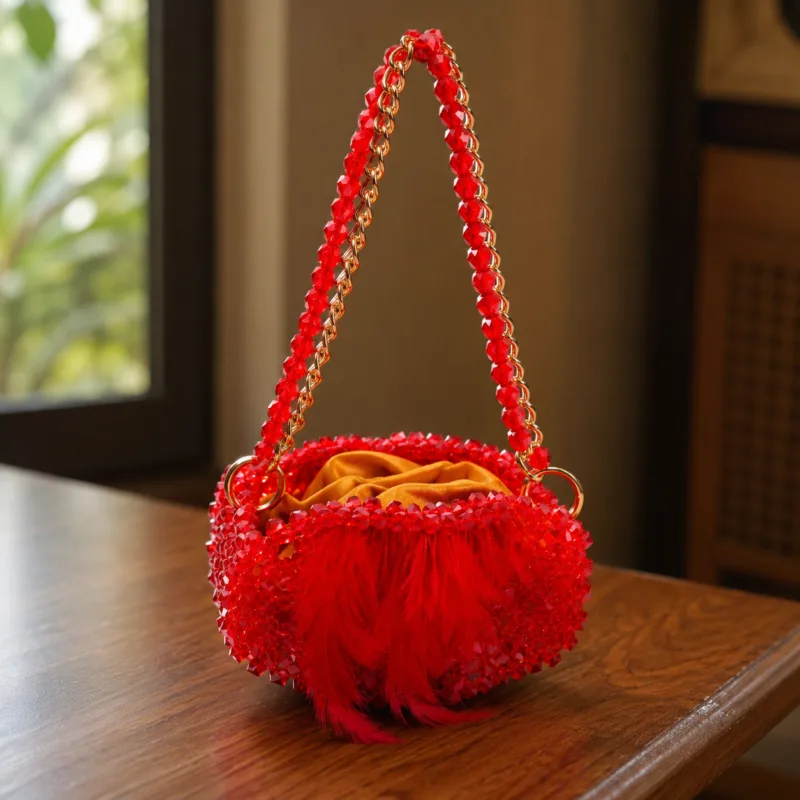Vue de profil du sac à main perlé rouge à plumes, posé sur une table en bois