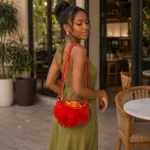 Mannequin portant en bandoulière le sac à main perlé rouge à plumes, robe vert olive