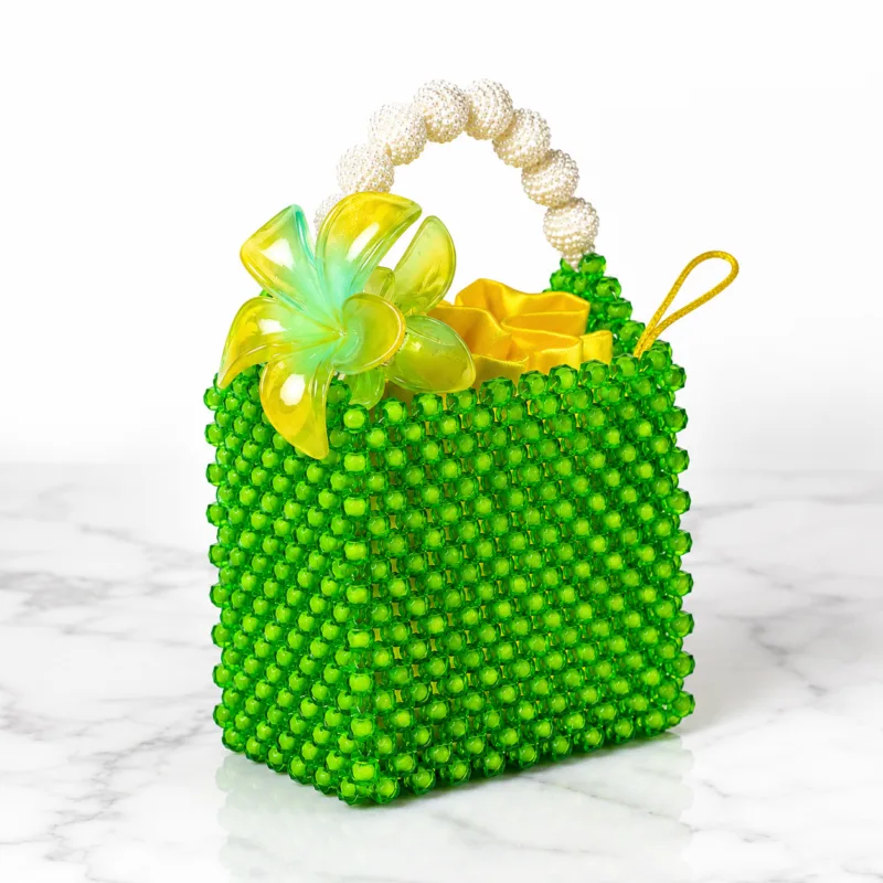 Sac Zawadi vu de face sur marbre blanc, perles vert émeraude, poignée en perles nacrées et fleur jaune décorative