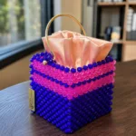 Vue de trois-quarts du sac à main perlé violet et rose, posé sur une table en bois